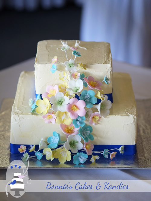 Vanilla sponge & banana cake with a white chocolate buttercream covering, and icing flowers coloured to suit a spring theme|  Bonnie’s Cakes & Kandies