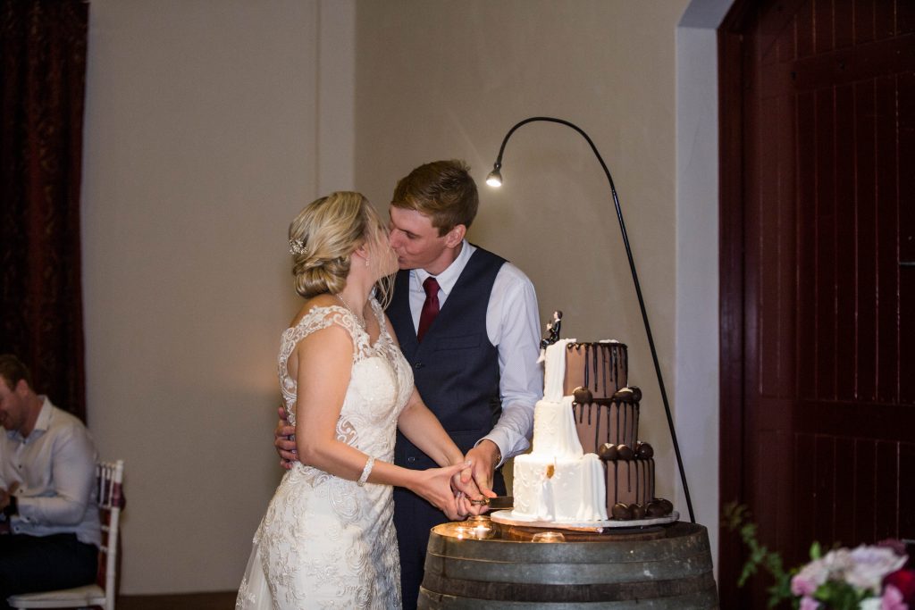 Bride and groom kissing as they cut their gluten free wedding cake by Bonnies Cakes and Kandies at Flaxton Gardens wedding venue